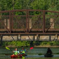 three people in single kayaks paddling under a bridge